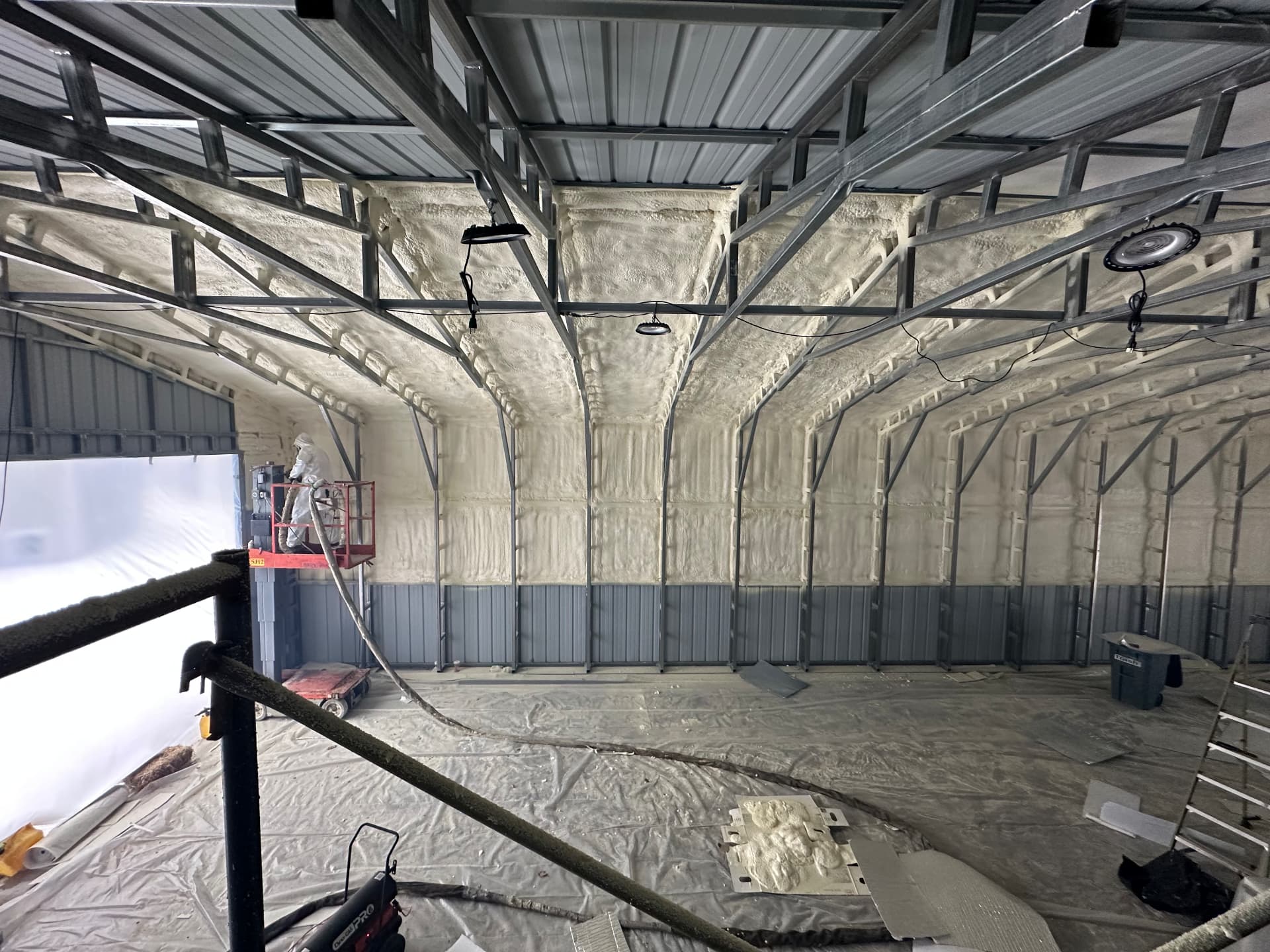 Spray foam insulation being applied to a steel building ceiling and walls