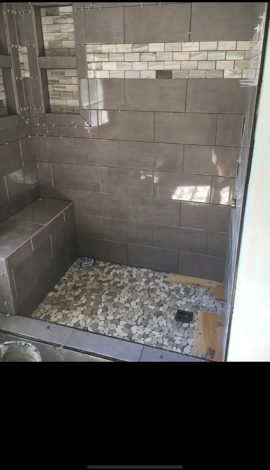 Custom tiled shower with built in bench, niche, and pebble floor